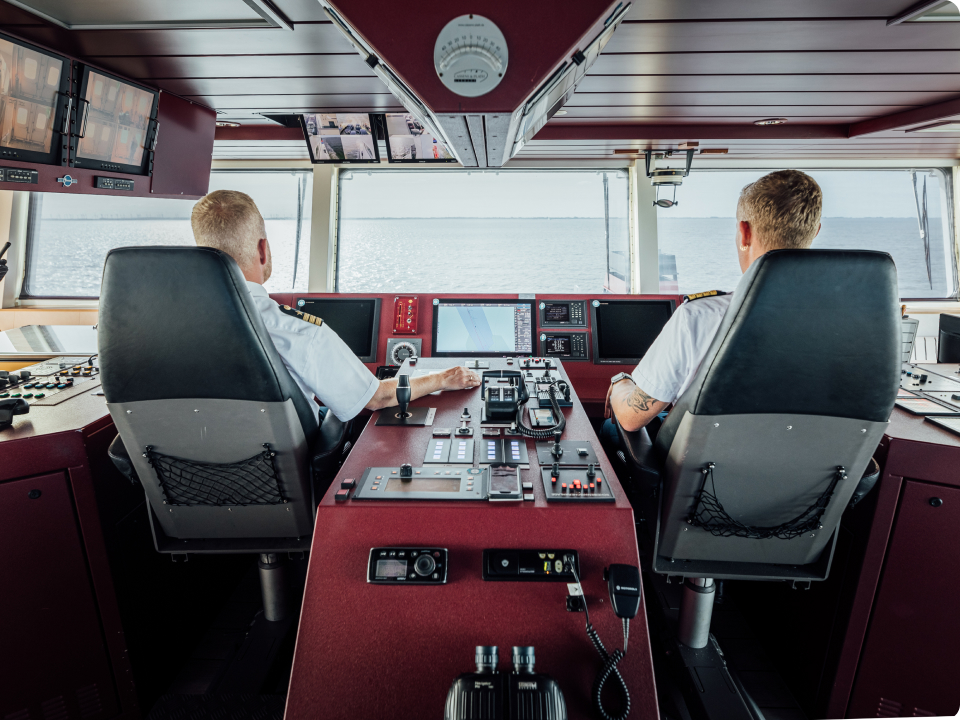 Ausblick aufs Meer aus einem Schiff heraus. Zwei Männer der Schiffsbesatzung sind von hinten auf ihren Plätzen zu sehen